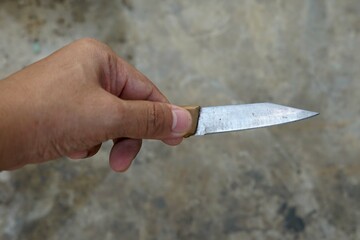 Man's hand holding a old knife with a cement baclgrounds.