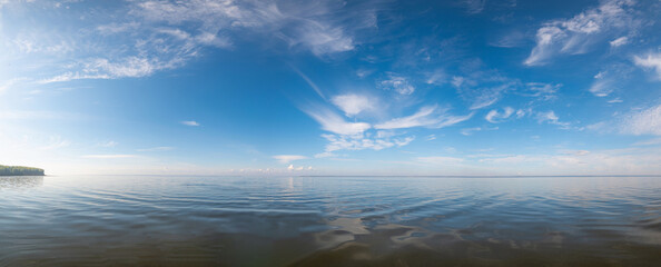 Panorama of the calm mirrored Kama River in Russia, Perm Krai, blue sky with clouds and the sun reflected in the water.