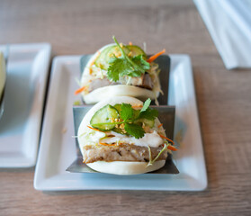 beautiful soft bao buns filled with pork belly, cucumbers, cilantro, coleslaw, and sauces at an asian restaurant