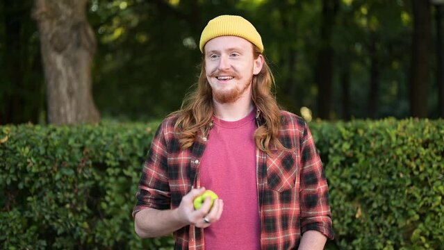 A young red-haired guy throws a green apple into the air, anticipating the pleasure of eating a ripe fruit. The image of a vegan and vegetarian