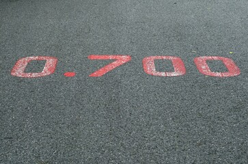 A red distance sign  numbers 0.700 KM  marken on surface the street in the parks