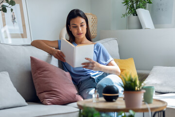Beautiful woman reading a book while essential oil aroma diffuser humidifier the air in living room at home - obrazy, fototapety, plakaty