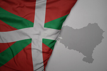 big waving national colorful flag and map of basque country on the gray background.