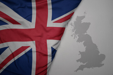 big waving national colorful flag and map of great britain on the gray background.