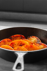 Fried apple, Pink Lady variety, in a cast iron frying pan. On a wooden chopping board in a kitchen. with selective colour