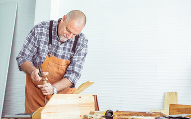 Senior Caucasian happy retired old male woodworker or carpenter wearing check shirt, holding hammer...