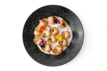Cooked grape snails in shells on a black plate isolated