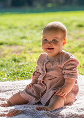 Portrait of a charming baby in a beige dress, The little girl is one year old. The child smiles. Sunny day in the park