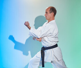 Black belt athlete doing formal exercises against a colored background with blue and green tint