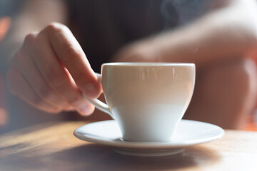 The man hand holding a white cap with tea or coffee in the restaurant.
