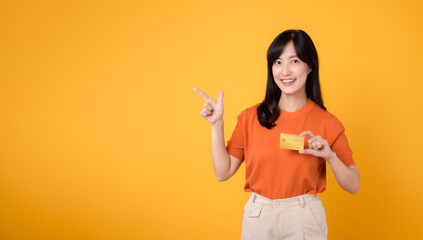 Successful businesswoman in her 30s, holding a credit card and pointing finger, making secure online transactions on yellow backdrop.