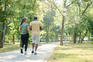 Rear view of multiethnic senior couple running together outdoors in the park