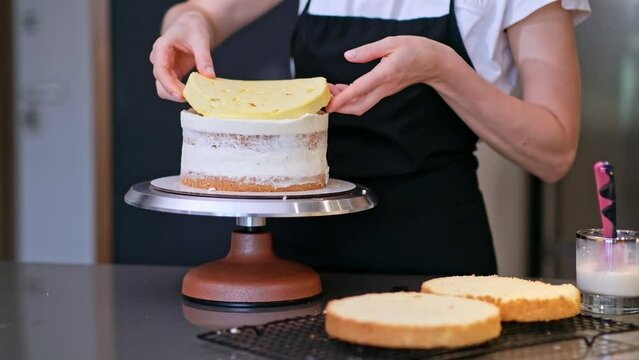 Professional confectioner in black apron connecting gluten free cake layers smeared with white cream skilled blonde woman working on handmade wedding pastry for client