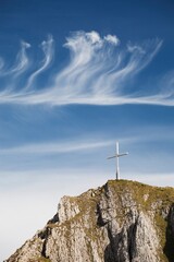 Fototapeta na wymiar Mountain Peak With A Cross On Top Against A Blue Sky With Clouds; Fussen, Germany