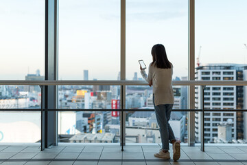 Woman use mobile phone over the big window inside business office tower