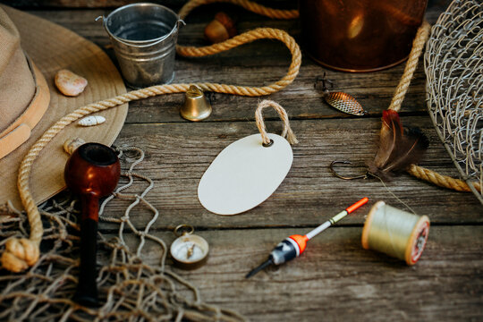 Fishing theme. Oval label with hooks, bucket, fishing buoy, compass and fish string on wooden background. Free space