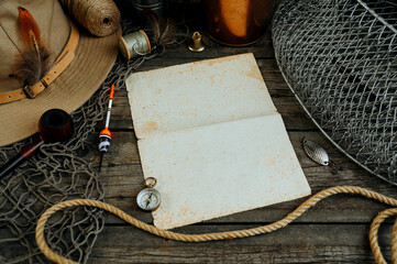 Vintage paper between fshing tackles, cap, net, bucket on a wooden board. Fishing concept background