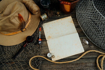 Vintage paper between fshing tackles, cap, net, bucket on a wooden board. Fishing concept background