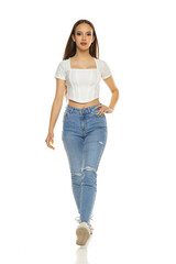 Young woman in white shirt, blue jeans and sneakers walk on a white background