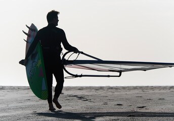 A Man Walking On The Beach Carrying A Kite Surfboard; Tarifa, Cadiz, Andalusia, Spain