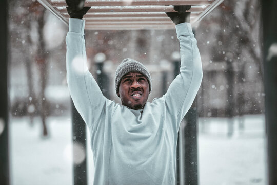 Young African American man doing the monkey bars exercise in an outdoor park during winter and snow