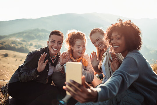 Young and diverse group of female friends taking a selfie on a smartphone while hiking in the mountains and hills