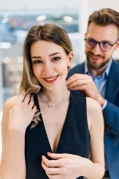 Beautiful couple enjoying in shopping at modern jewelry store. Young woman try it out gorgeous necklace and earrings. Fashion style and elegance concept.