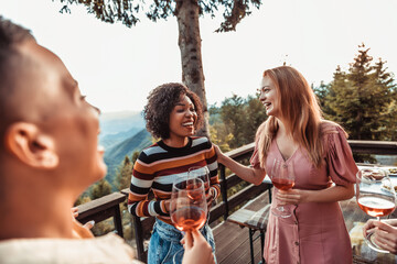Young and diverse group of female friends having wine on a balcony of a cabin house in the forest