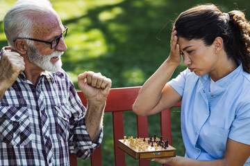 Senior man and nurse playing chess in park