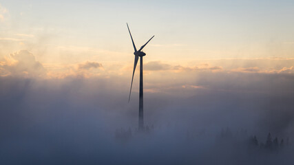 Wind turbine on a mountain above the clouds with a dramatic sky during sunset