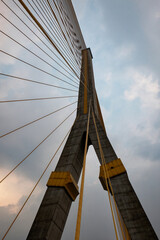 A towering suspension bridge, with concrete pillars and steel cables, cloudy sky.