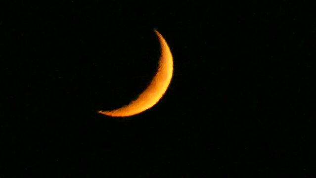 Dark night sky and orange and yellow crescent moon with visible fragments of craters - natural view before moonset in real time. Topics: astronomy, optical phenomenon, atmosphere, cosmos, science