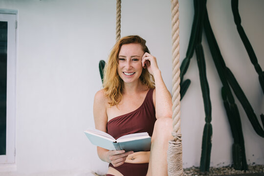 Cheerful young woman reading book on swing