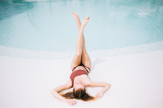 Slim woman lying on poolside with legs up