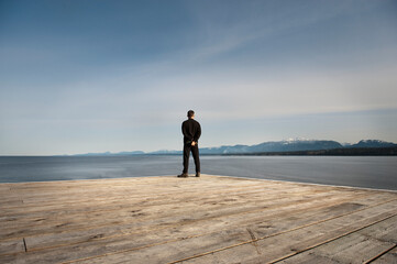 A Man Stands At The End Of A Wooden Dock Looking Out Over The Ocean; Chrome Island British Columbia Canada