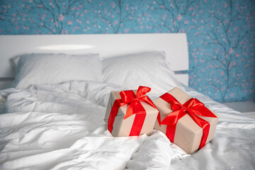 Two gift boxes with red ribbon and craft paper lie on the bed in the bedroom