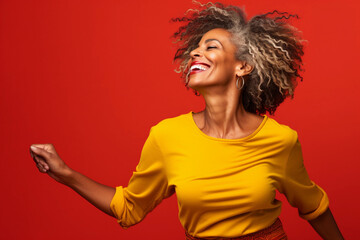 Fashion senior woman wearing yellow shirt and dancing isolated on red background