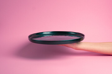 Empty green plate held in hand. Pink background.