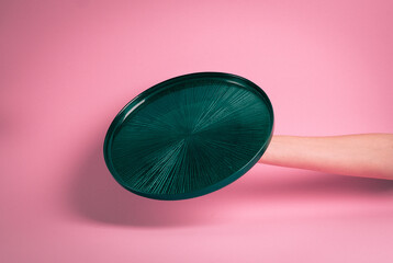Empty green plate held in hand. Pink background.