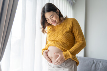 Pregnant asian woman holds hands on belly touching her baby caring about her health Beautiful happy pregnant woman tender mood photo of pregnancy