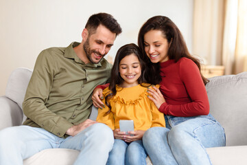 Happy Arabic family holding using mobile phone sitting at home