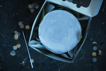 Small bento cake in a white gift box on the dark moody blue background. Flat lay. Birthday space cake for one person with a space for a free text on top