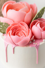 Birthday cake with white cream cheese frosting decorated with pink chocolate flowers on the wooden cake stand. Anniversary cake for a woman