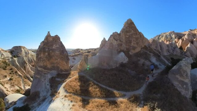 Tourist woman trekking in Red Valley Park at sunset in Cappadocia of Turkey. The soft, rust-colored rock formations, illuminated by the warm sunlight, create a mesmerizing backdrop for her journey.