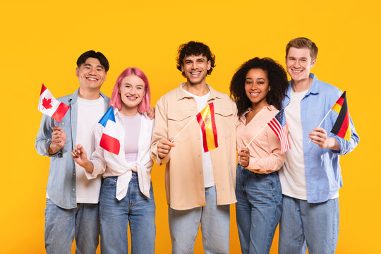 Happy multiracial people holding different countries flags and smiling at camera, standing on yellow background