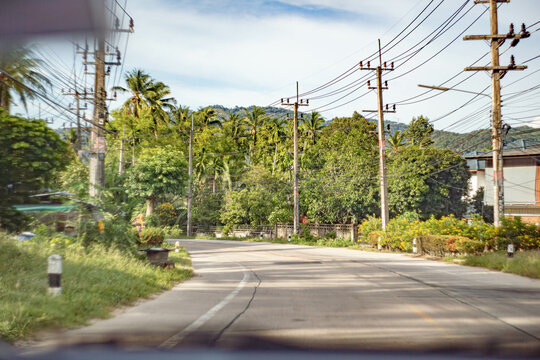 A Rural Road In Thailand With Palm Trees, Powerlines Anfd Mountains In The Distance