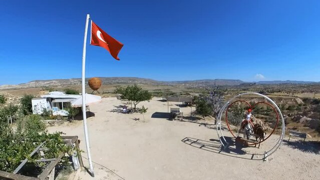 Woman standing at Devrent Valley lookout in Turkey with flag, surrounded by the magical ambiance of Cappadocian imagination valley, where the rocks come to life with her interpretations.