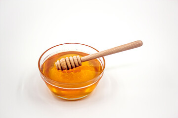 Glass bowl full of honey and wooden honey spoon inside the honey. Photograph.