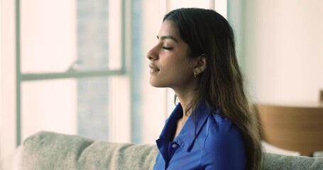 Close up calm young Indian woman rest on sofa with eyes closed, takes deep breath of fresh conditioned air, enjoying relaxation time alone at home, do meditation practice, relieving stress or fatigue