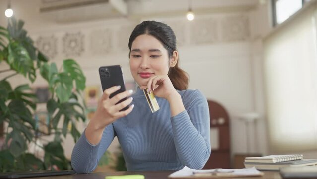Asian woman using credit card for online payment with laptop while sitting at the living room. online shopping Pay by credit card via electronic wallet. .